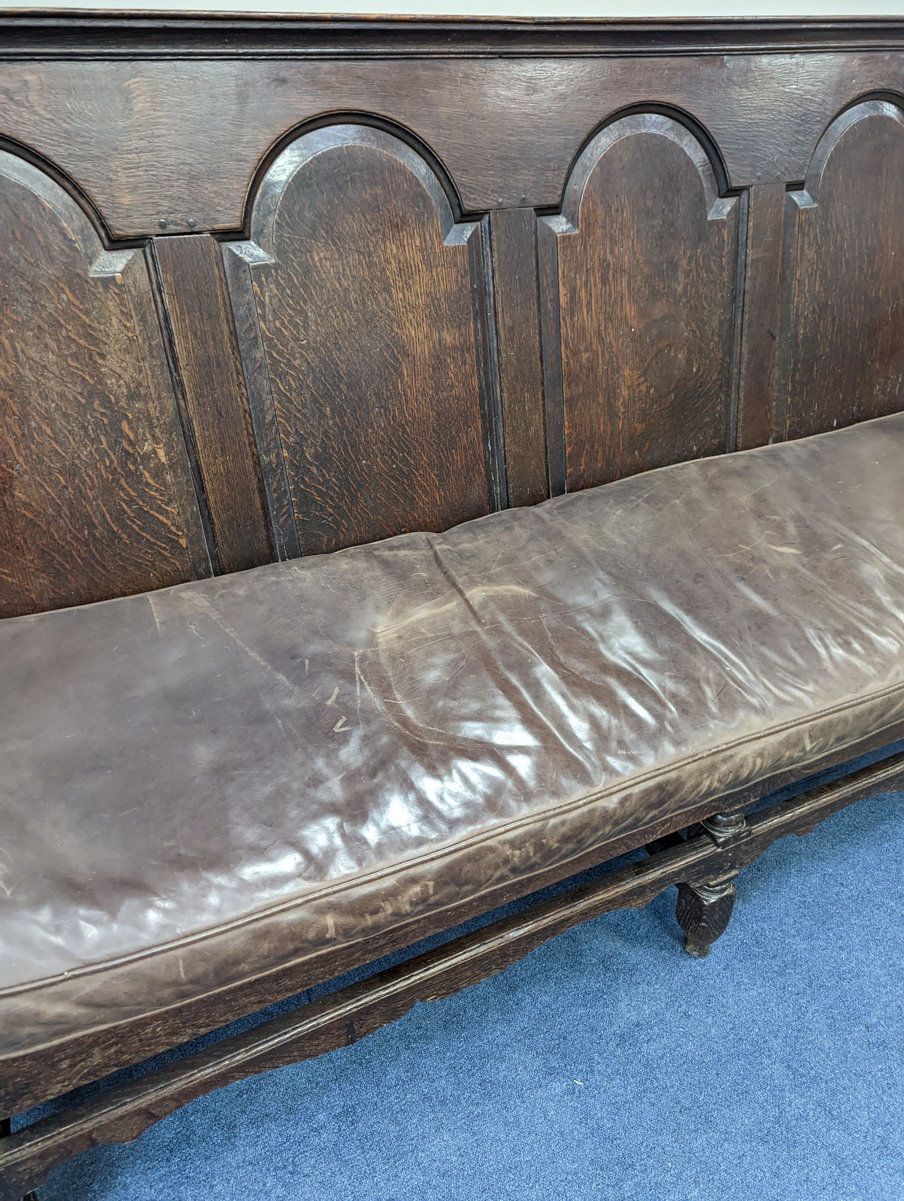 A mid 18th century panelled oak settle with leather squab seat, length 185cm, depth 77cm, height 114cm